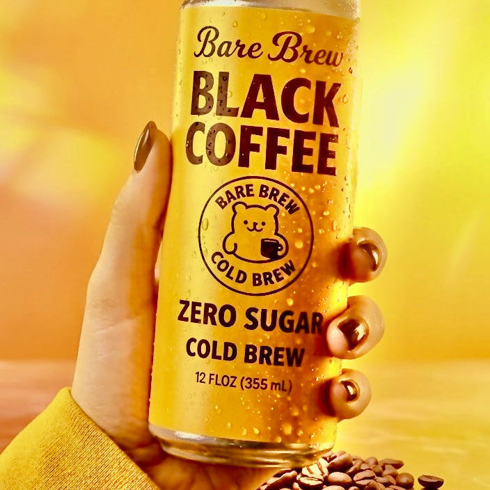 Can of Bare Brew Black Coffee Zero Sugar Cold Brew held by a hand with coffee beans on a yellow background